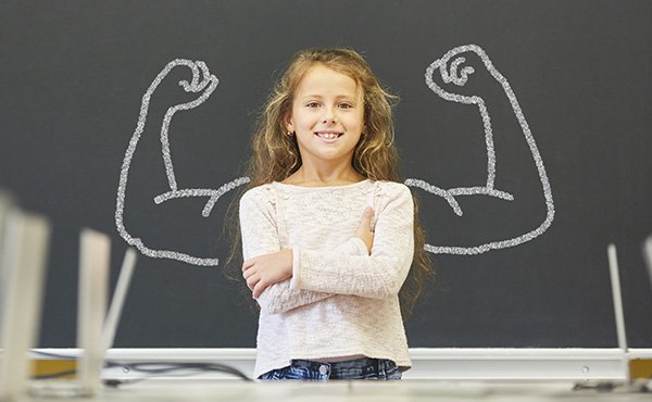 Mädchen in Schule steht vor Tafel mit Muskeln