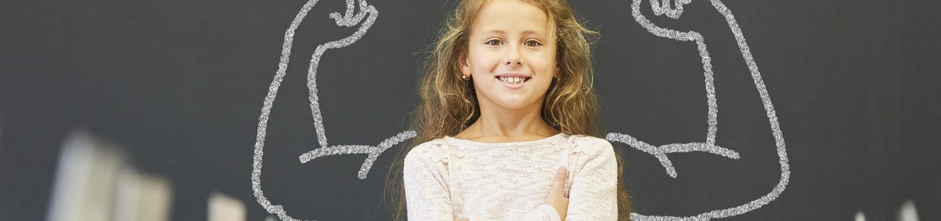 Mädchen in Schule steht vor Tafel mit Muskeln Lächelndes Mädchen in der Schule steht vor einer Tafel mit Muskeln aus Kreide